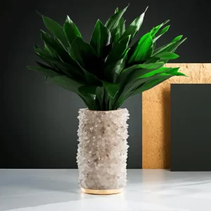 Gold leaf metal vase with white quartz crystals, decorated with green leafy plant in studio setting.