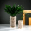 A pair of Quartz Flower Pots, medium and large sizes, adorned with lush green leaves, showcasing their harmonious design and warm gold leaf finish.