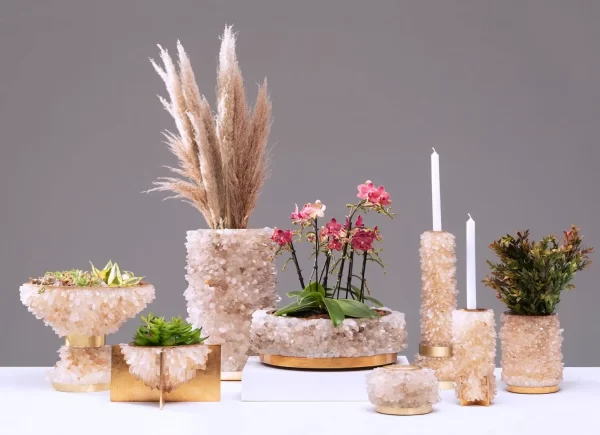 Composition of white quartz vases, gold-plated candelabras and centerpieces with flowers, candles, and wheat grass on neutral background