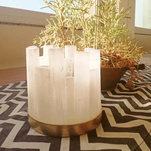 Alexxa IV Natural Stone Candle Holder in gold leaf, placed next to a cactus in a well-lit room near a window, showcasing its handcrafted selenite and metal frame.
