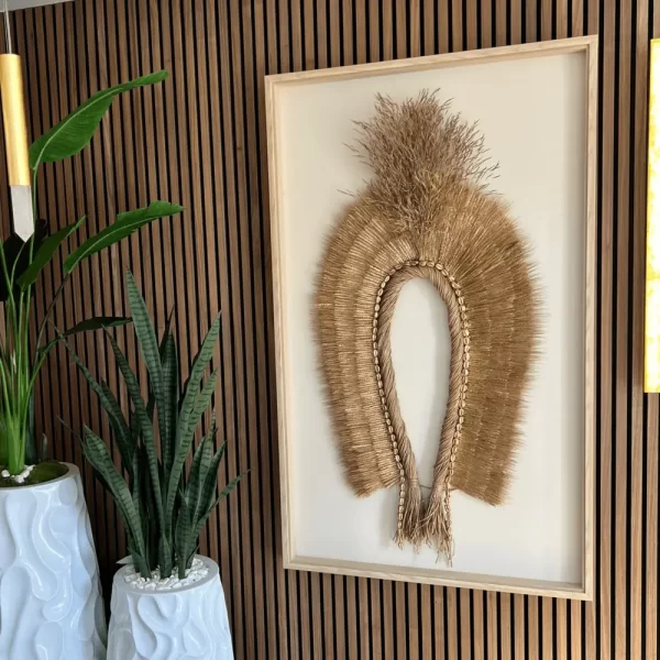 Indigenous Natural Fiber Headdress Antunes with Wheat and Shells in Freijó-Colored Frame on Textured Wood Wall with Snake Plant Vases