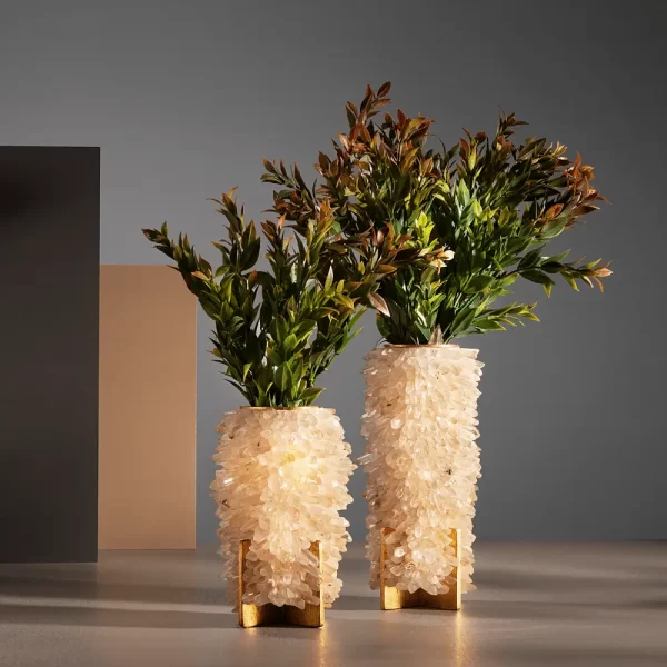 Close-up at a pair of Sculptural Small Vases, White Quartz, Desiree, in small and medium sizes, adorned with lush foliage. The vases feature a fine Brazilian craftsmanship with an accurate selection of Crystal Quartz, perfect for interior design projects.