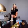 A woman posing beside a luxurious white quartz candle holder on a dark table, surrounded by high-end decorative elements like a succulent centerpiece, books, and modern accents.