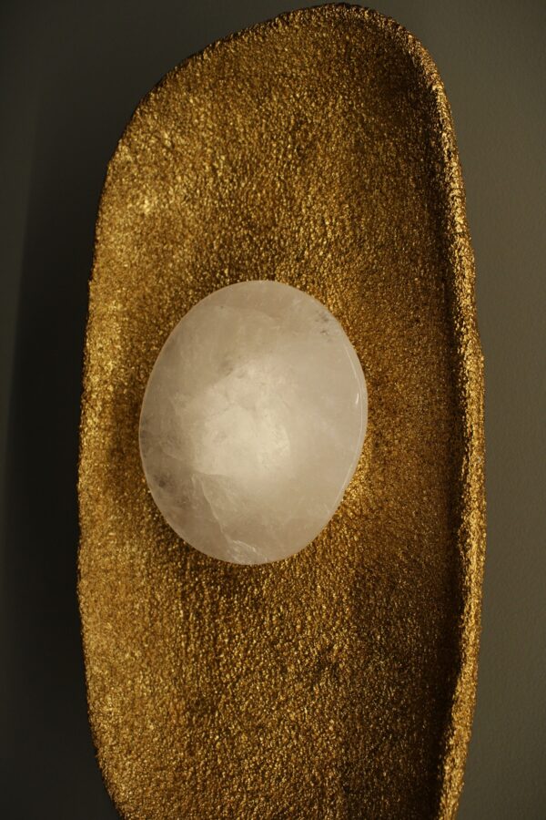 Wall light with a golden textured base and a translucent spherical crystal, combining raw materials with refined craftsmanship.