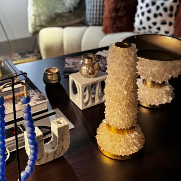 A cozy, elegant interior featuring a white quartz candle holder and matching bowl with gold accents on a dark table, styled with blue beads, books, and modern decor pieces.