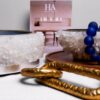 Close-up of a white quartz centerpiece with silver leaf details, accompanied by blue beads and gold decorative chains on a modern minimalist table setting.